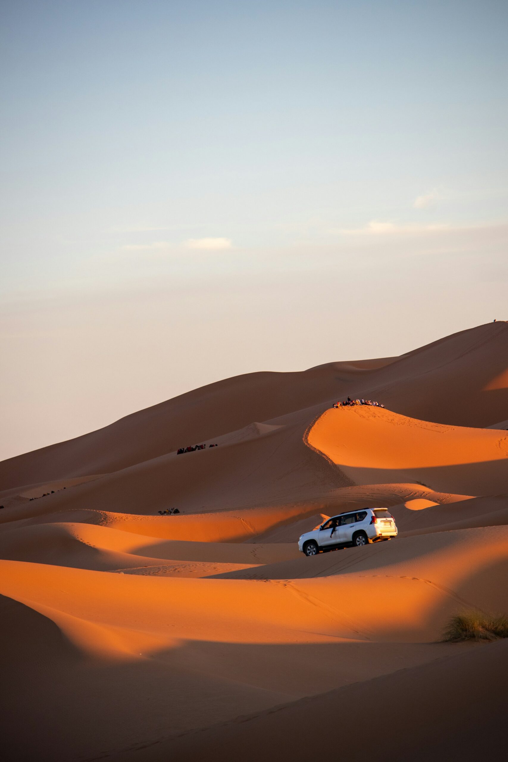 Off-road vehicle driving through the desert with sand dunes in the background