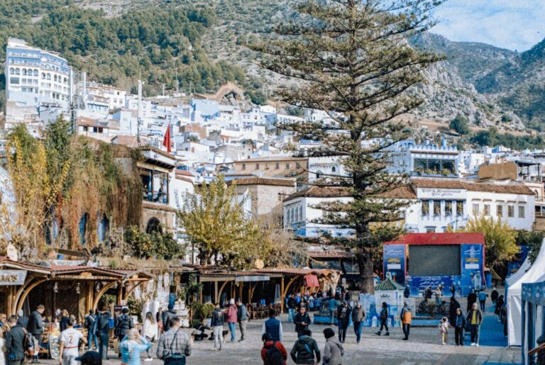 People in a lively town square surrounded by blue buildings in Chefchaouen