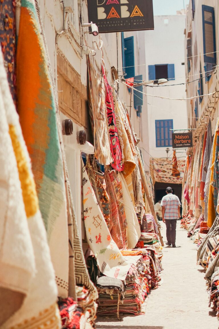 Person walking down a narrow alley in Essaouira lined with colourful rugs