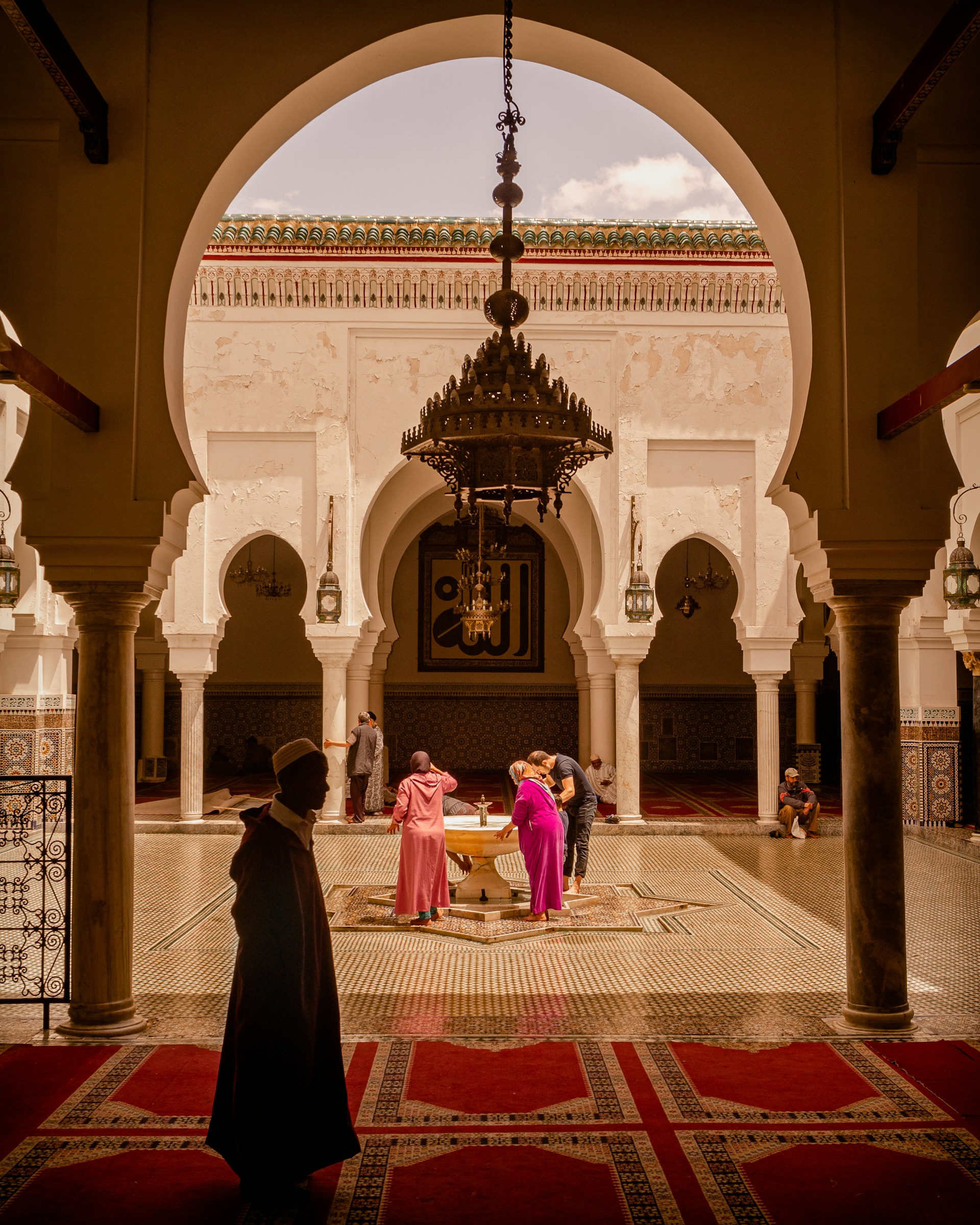 Visitors beside a zellige fountain in a historic courtyard in Fes