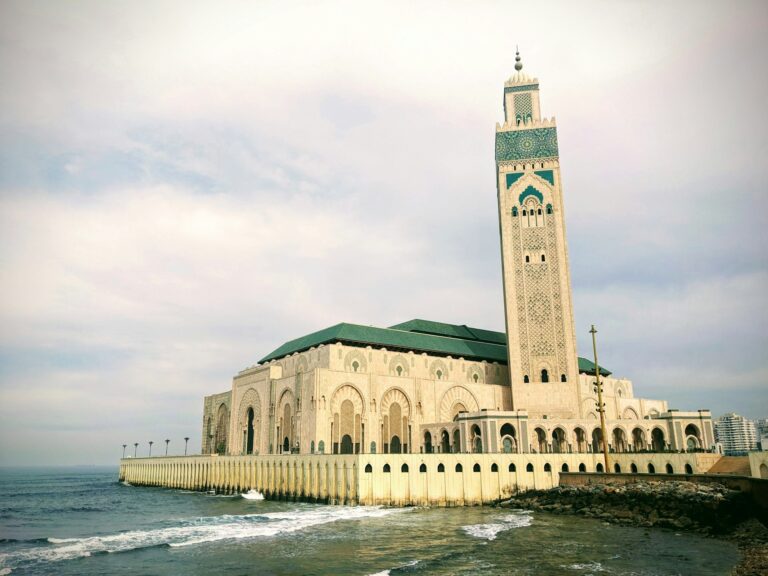 Large white mosque with a green-tiled roof beside the Atlantic Ocean in Casablanca