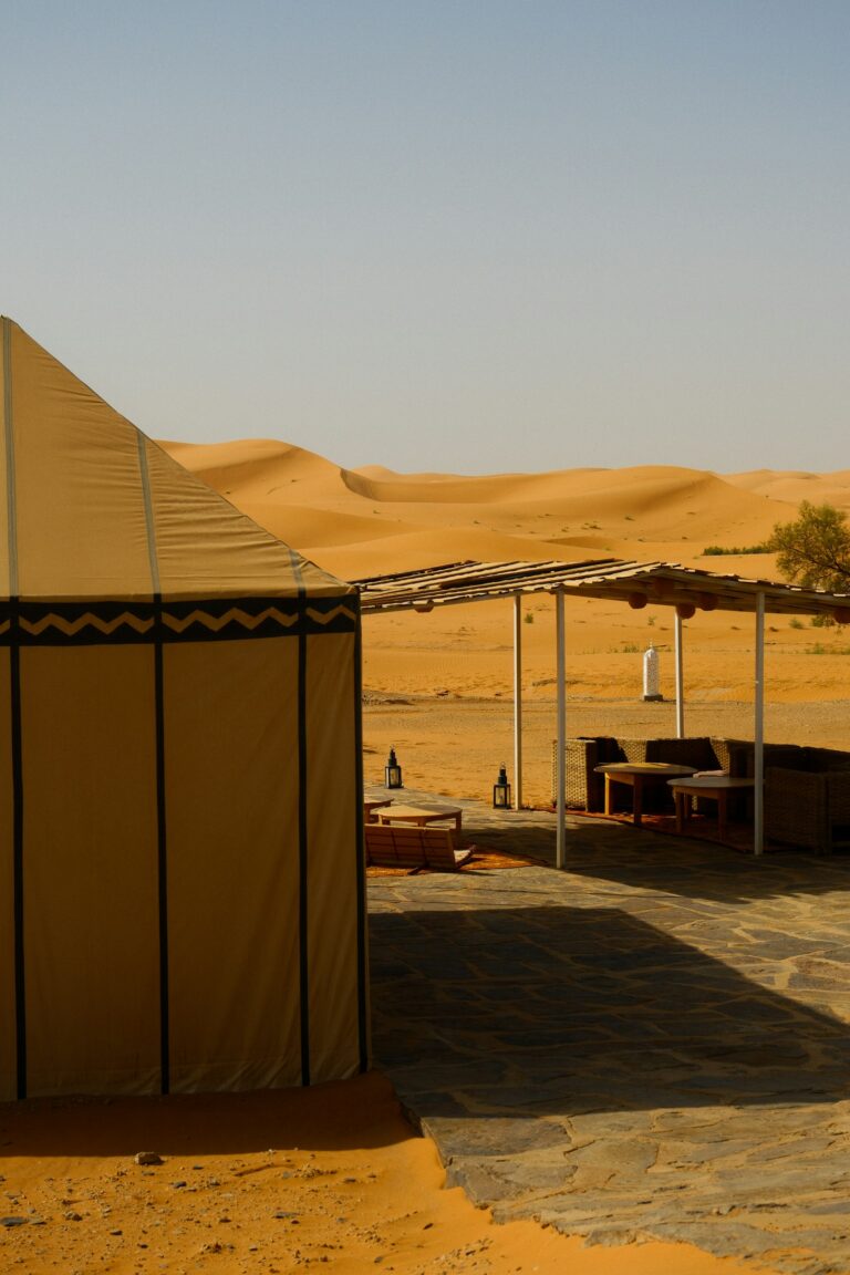 Desert camp with white tents and an outdoor seating area among the dunes