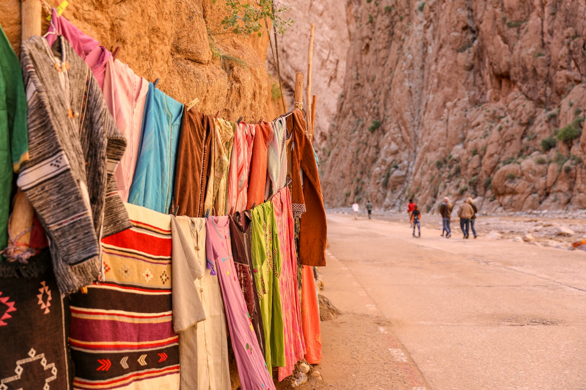Textiles displayed beside the towering rock walls of the Todra Gorge