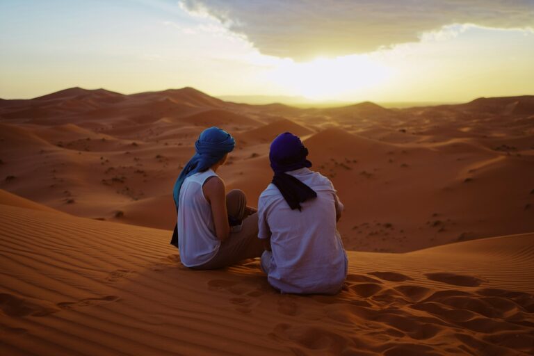 Two travelers sitting on a sand dune watching the Sahara landscape